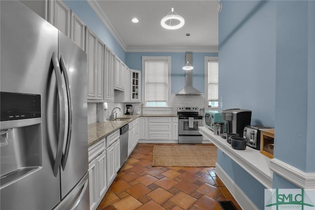 kitchen with a sink, decorative backsplash, appliances with stainless steel finishes, crown molding, and wall chimney range hood