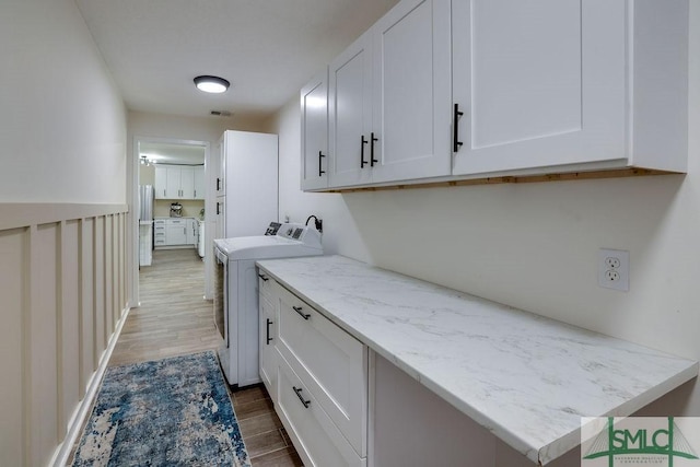 clothes washing area featuring wood finished floors, cabinet space, independent washer and dryer, and visible vents