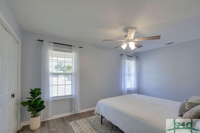 bedroom with visible vents, a textured ceiling, wood finished floors, a closet, and ceiling fan