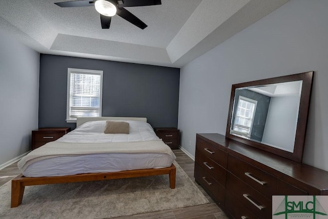 bedroom featuring a tray ceiling, wood finished floors, baseboards, and a textured ceiling