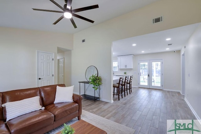 living area with visible vents, light wood-style floors, vaulted ceiling, and french doors