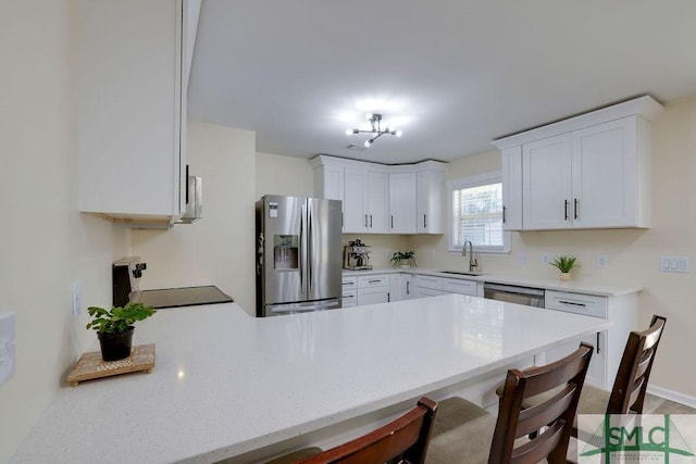 kitchen with a breakfast bar, a peninsula, white cabinets, stainless steel appliances, and a sink