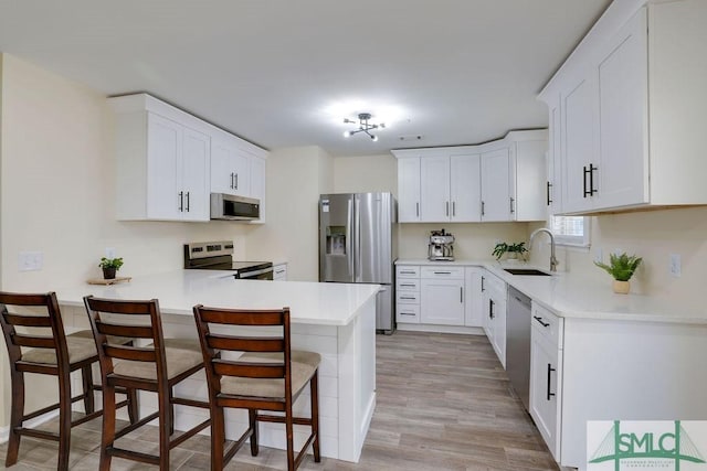 kitchen with a peninsula, a sink, stainless steel appliances, light countertops, and a kitchen breakfast bar