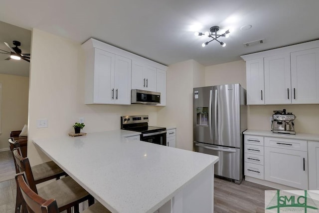 kitchen featuring visible vents, a kitchen bar, light wood-type flooring, light countertops, and appliances with stainless steel finishes