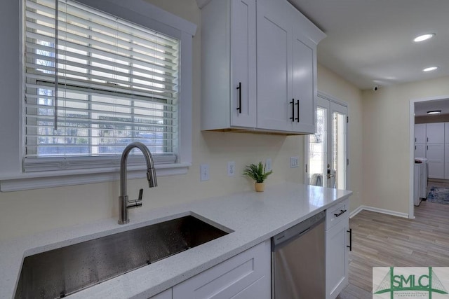 kitchen with light stone counters, white cabinetry, light wood-style flooring, a sink, and stainless steel dishwasher