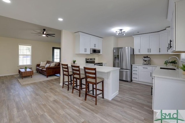 kitchen with open floor plan, light countertops, a kitchen bar, appliances with stainless steel finishes, and a sink