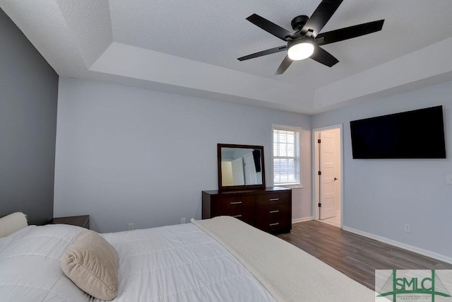 bedroom with a ceiling fan, baseboards, a tray ceiling, dark wood-type flooring, and a textured ceiling