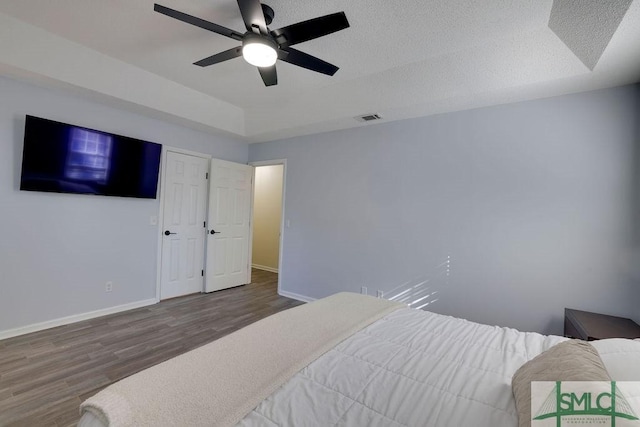 bedroom with visible vents, a tray ceiling, a textured ceiling, wood finished floors, and baseboards