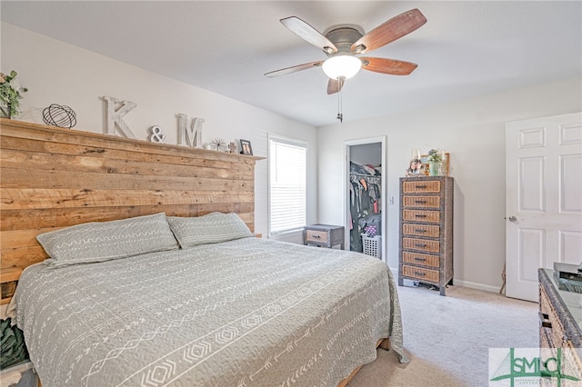 bedroom featuring a walk in closet, baseboards, light colored carpet, a closet, and a ceiling fan