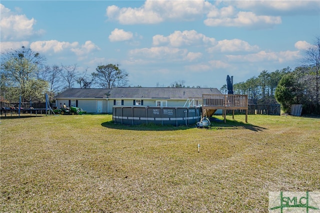 rear view of property with an outdoor pool, a wooden deck, a trampoline, and a lawn