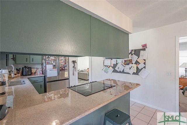 kitchen featuring light tile patterned floors, freestanding refrigerator, a sink, green cabinets, and black electric stovetop