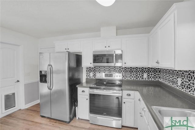 kitchen featuring dark countertops, stainless steel appliances, white cabinets, light wood finished floors, and decorative backsplash