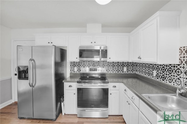 kitchen with appliances with stainless steel finishes, white cabinetry, light wood-type flooring, and a sink