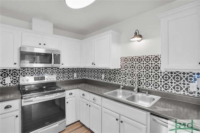 kitchen with dark countertops, white cabinetry, stainless steel appliances, and a sink