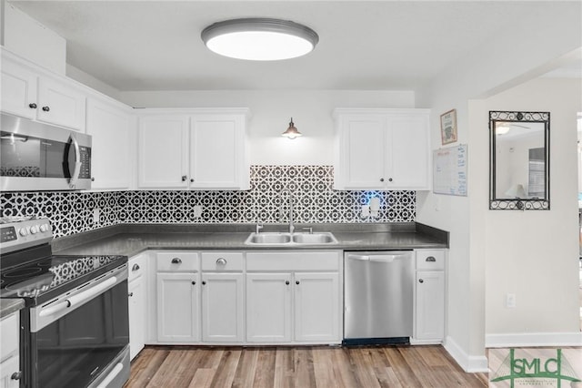 kitchen with dark countertops, stainless steel appliances, light wood-style floors, white cabinetry, and a sink