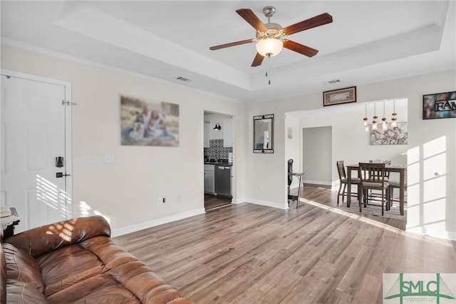 living area featuring a ceiling fan, wood finished floors, baseboards, visible vents, and a tray ceiling