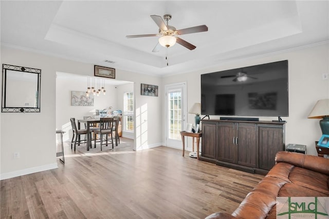 living area featuring a raised ceiling, light wood-style floors, visible vents, and baseboards