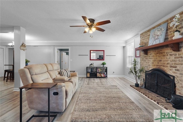 living area with a brick fireplace, baseboards, ceiling fan, light wood-style flooring, and a textured ceiling