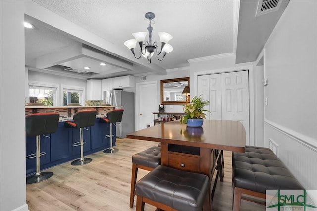 dining room featuring light wood-type flooring, visible vents, a notable chandelier, crown molding, and a dry bar