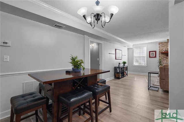 dining space with light wood-type flooring, visible vents, a textured ceiling, and an inviting chandelier