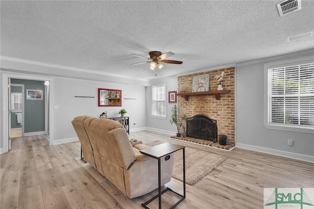 living area with visible vents, light wood-style floors, a brick fireplace, and a healthy amount of sunlight