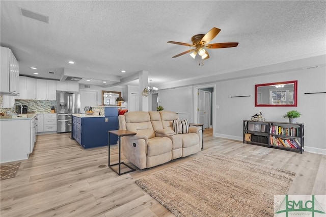 living area featuring light wood finished floors, ceiling fan with notable chandelier, and a textured ceiling