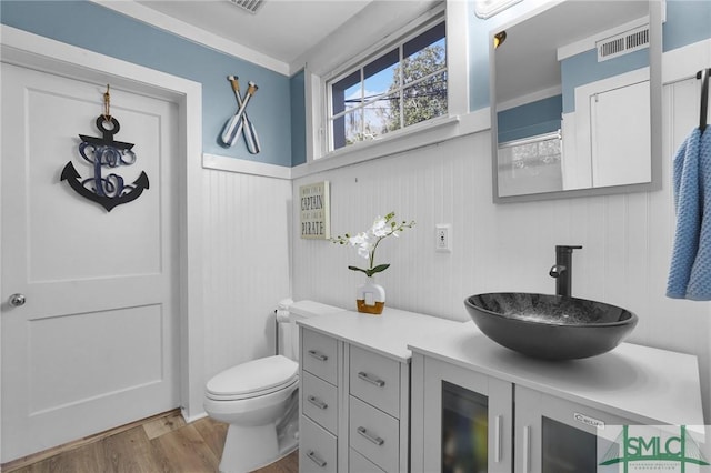 bathroom with visible vents, a wainscoted wall, toilet, wood finished floors, and vanity