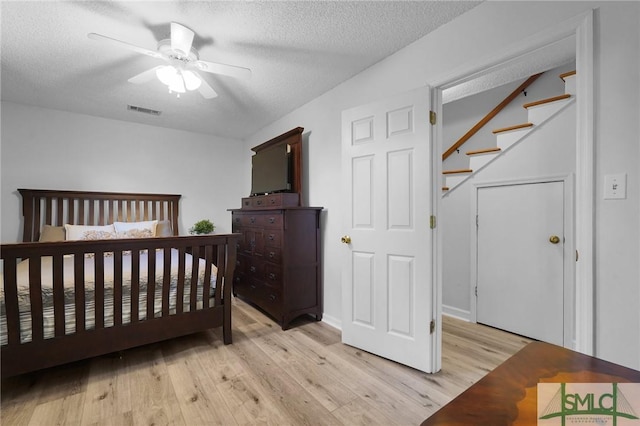 bedroom with visible vents, light wood-style flooring, a textured ceiling, and ceiling fan