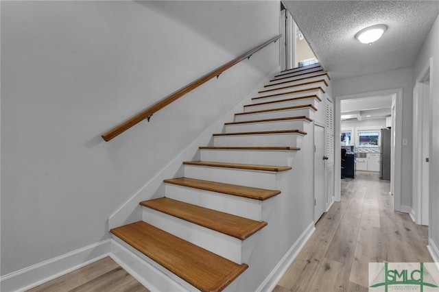 stairs with wood finished floors, baseboards, and a textured ceiling