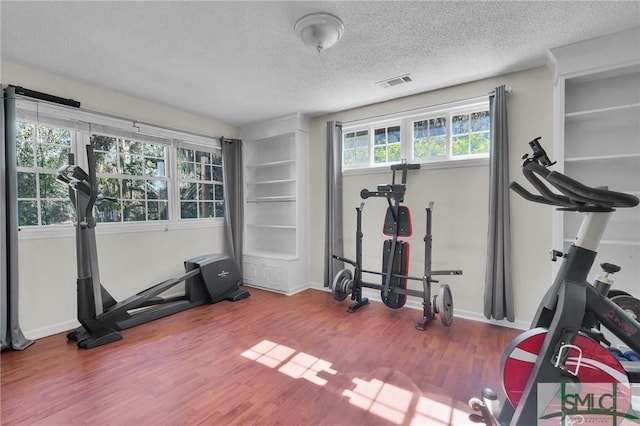 exercise room with visible vents, baseboards, a textured ceiling, and wood finished floors