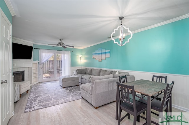 living room with wainscoting, a brick fireplace, ornamental molding, and wood finished floors