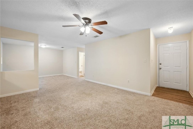 carpeted empty room with visible vents, a ceiling fan, baseboards, and a textured ceiling