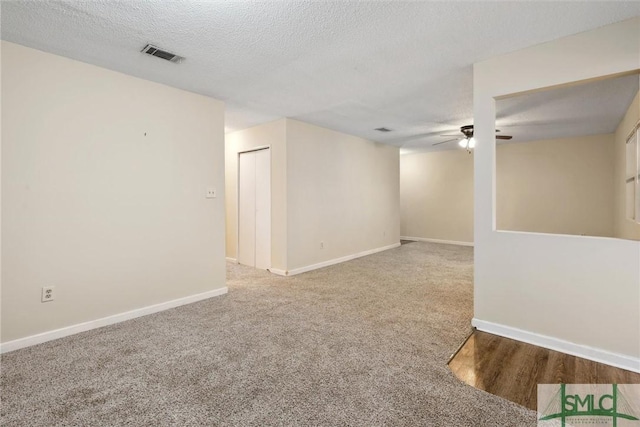 carpeted spare room with visible vents, baseboards, a textured ceiling, and a ceiling fan