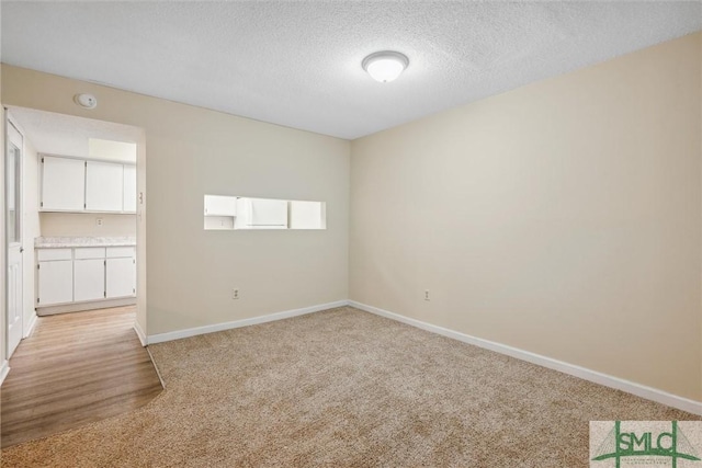 unfurnished room featuring baseboards, a textured ceiling, and light carpet