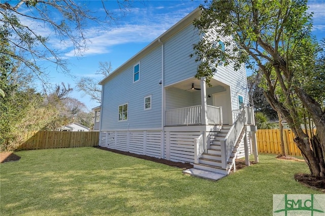 back of house featuring stairs, a ceiling fan, a lawn, and a fenced backyard