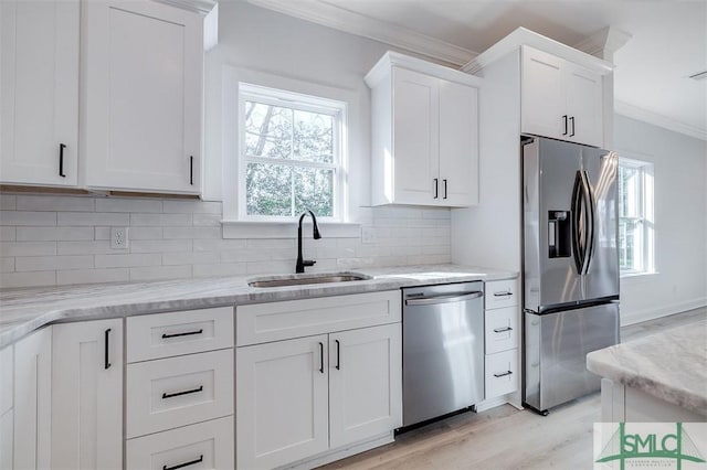 kitchen with ornamental molding, a sink, backsplash, appliances with stainless steel finishes, and white cabinets