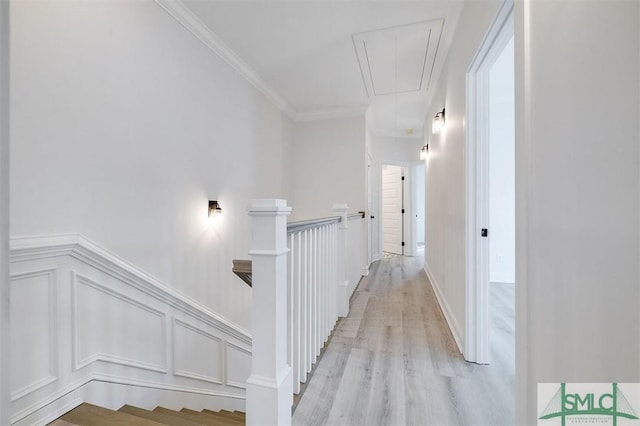 hallway featuring a wainscoted wall, attic access, light wood-style flooring, ornamental molding, and an upstairs landing