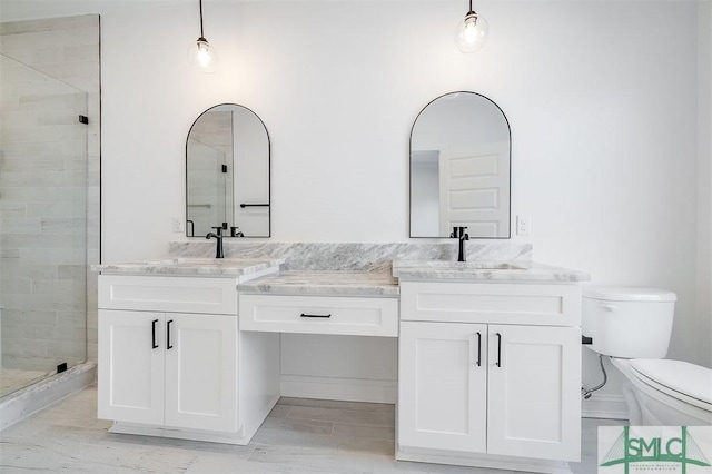 bathroom featuring double vanity, a shower stall, toilet, and a sink