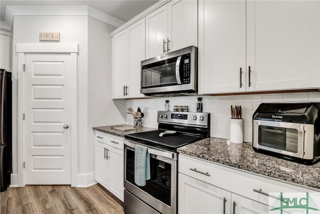 kitchen with dark stone countertops, stainless steel appliances, light wood-style floors, and decorative backsplash