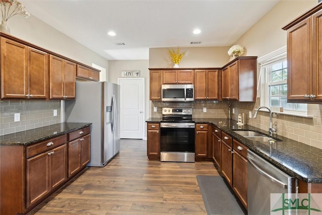 kitchen featuring visible vents, dark stone counters, a sink, dark wood-type flooring, and appliances with stainless steel finishes