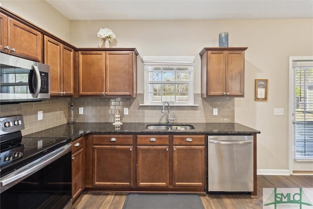 kitchen featuring dark wood-style flooring, dark stone countertops, stainless steel appliances, and a sink