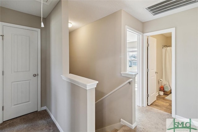 hallway featuring visible vents, baseboards, carpet, attic access, and an upstairs landing