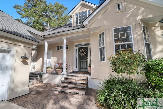 view of exterior entry with stucco siding, a porch, and a shingled roof