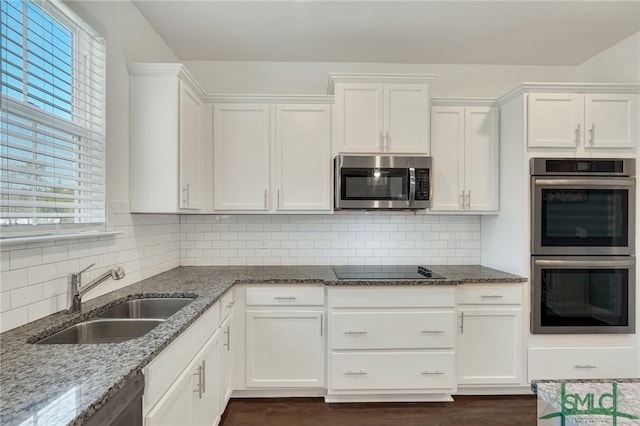 kitchen with a sink, backsplash, white cabinetry, stainless steel appliances, and light stone countertops