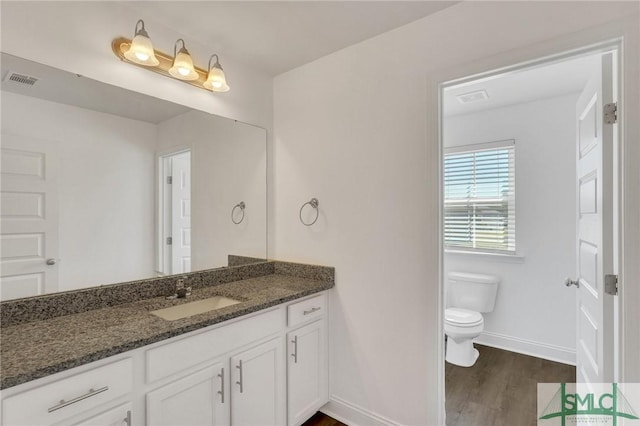 bathroom featuring visible vents, baseboards, toilet, wood finished floors, and vanity