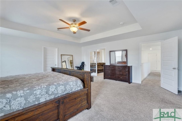 bedroom with visible vents, light carpet, a raised ceiling, a ceiling fan, and baseboards