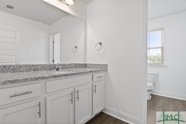 bathroom with vanity, toilet, baseboards, wood finished floors, and visible vents