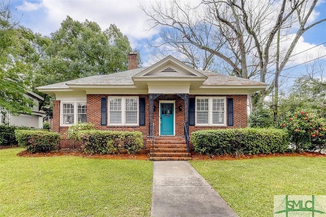 bungalow with a front lawn, brick siding, and a chimney