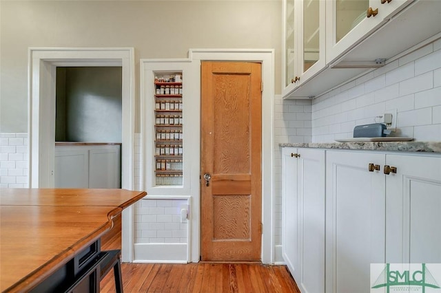 kitchen with white cabinetry, tasteful backsplash, glass insert cabinets, and light wood-type flooring