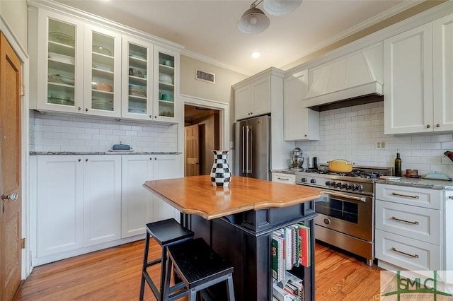 kitchen with visible vents, custom range hood, premium appliances, light wood-style floors, and crown molding